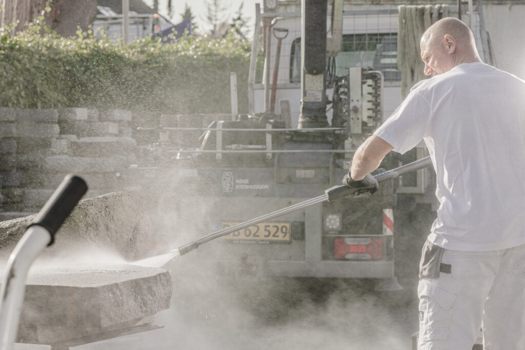 Mand renser mindesten med højtryksrenser foran lastbil.