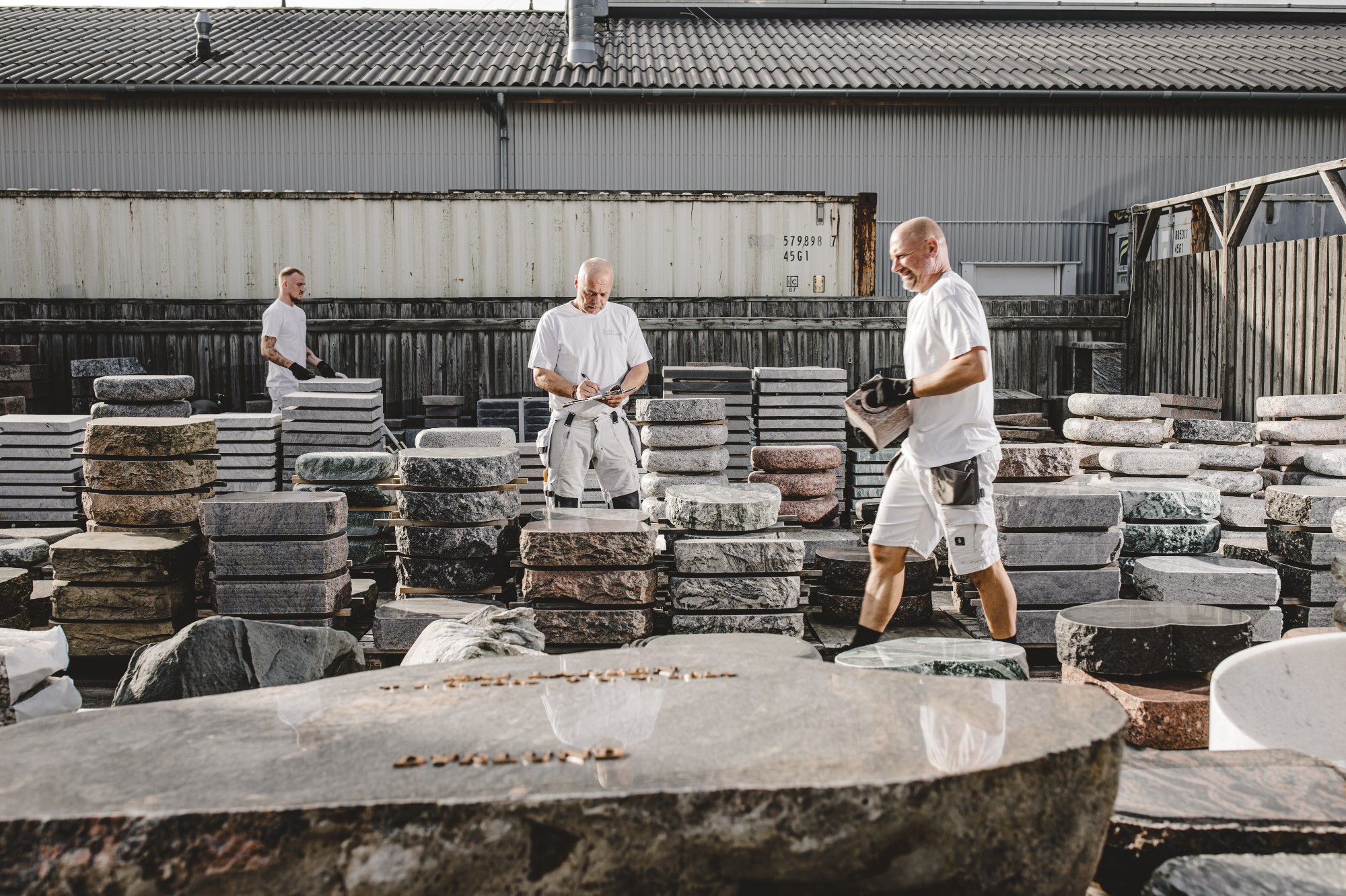 Stenhuggere arbejder i udendørs lager med mange mindesten og natursten.
