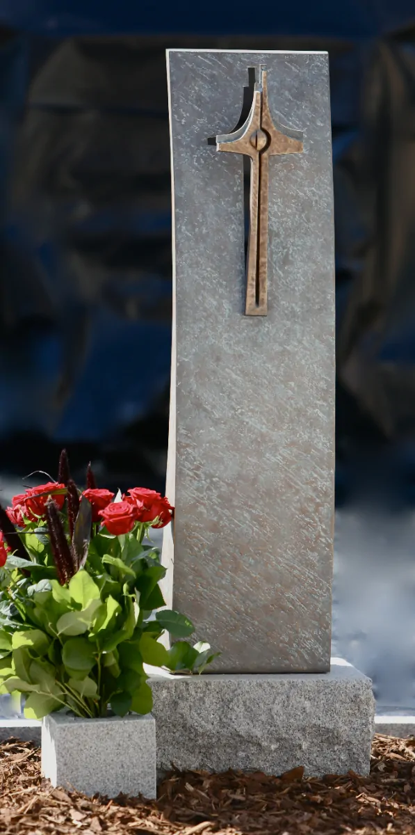 Unik mindesten i grå natursten med et bronze kors og friske røde roser.